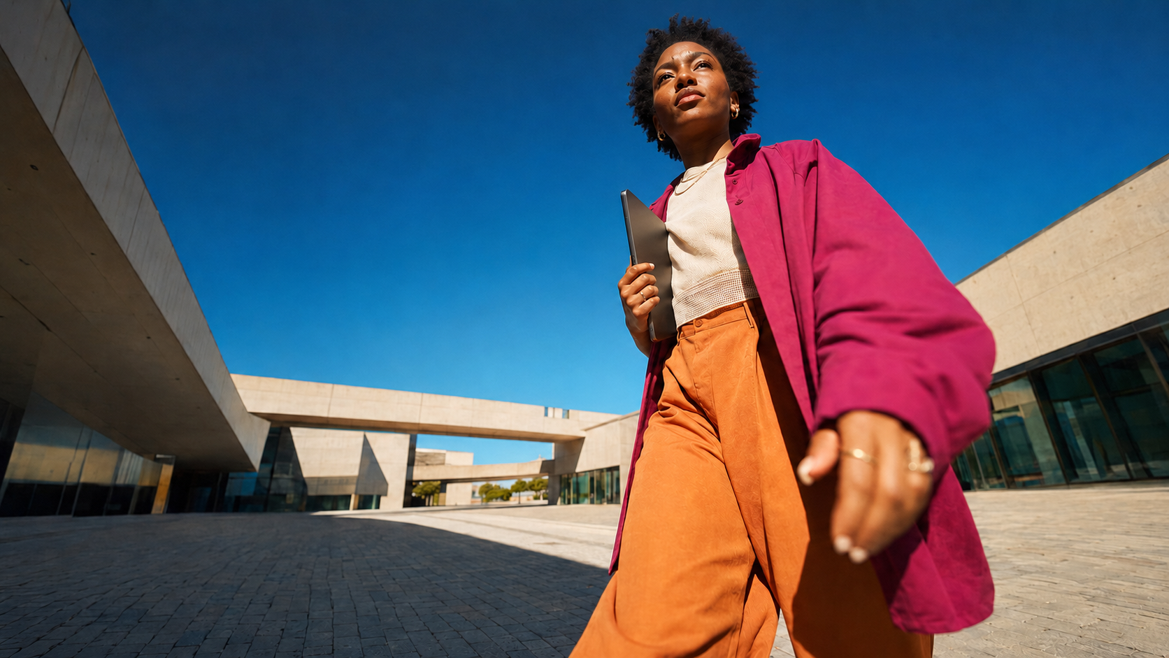 A person carrying a laptop through a modern architectural plaza